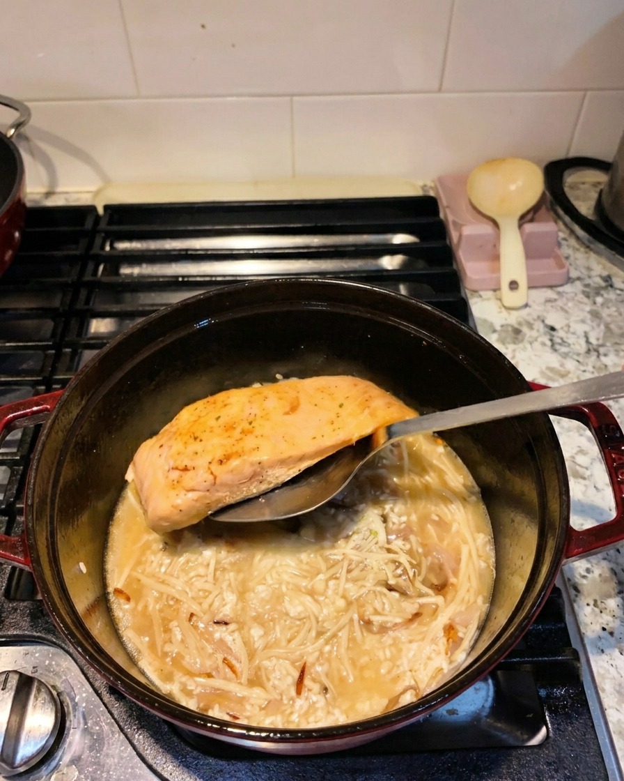 Una espátula metálica colocando un filete de salmón sellado en una olla con arroz, setas y líquido.