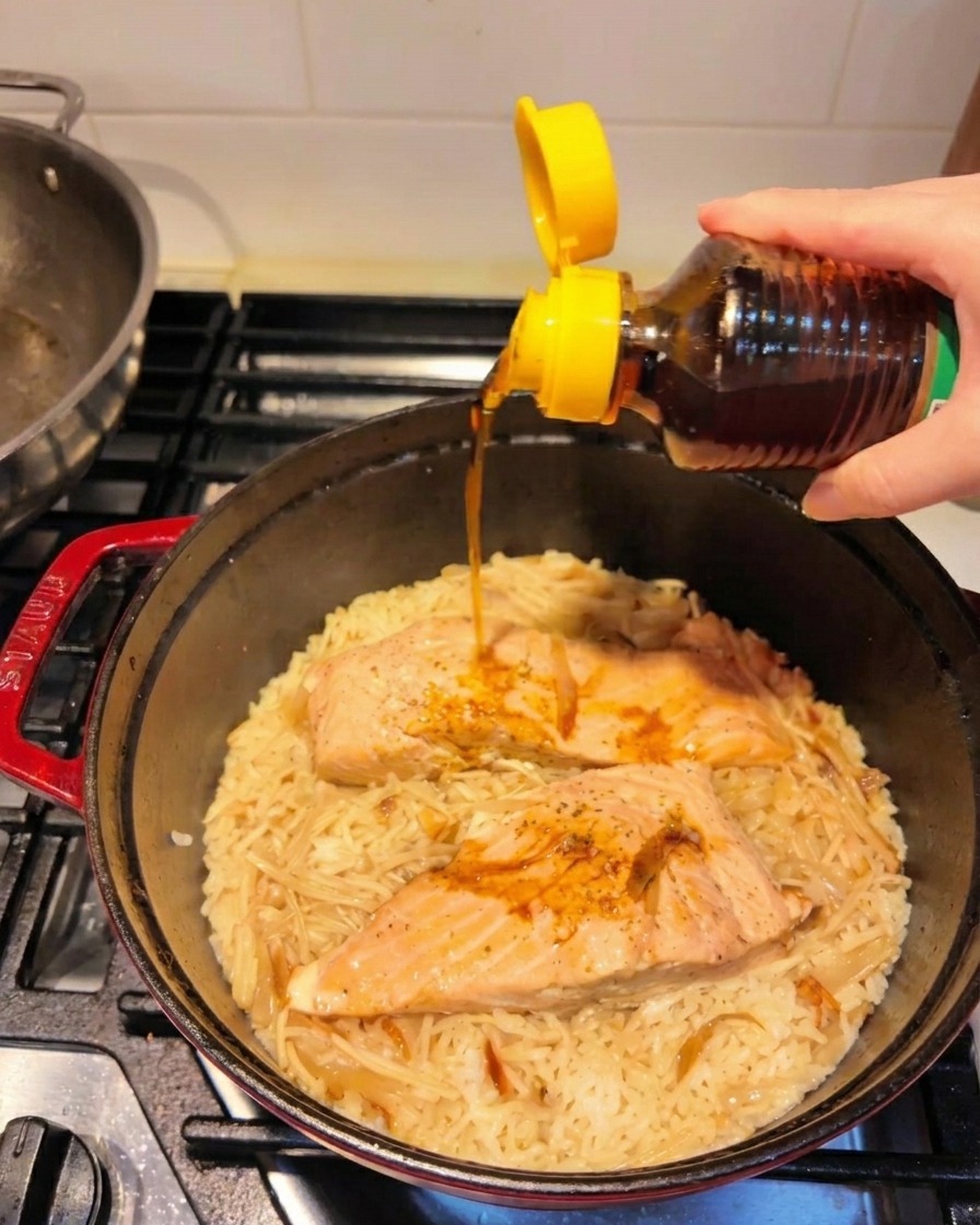 Aceite de sésamo tostado vertiéndose sobre el salmón y el arroz terminados.