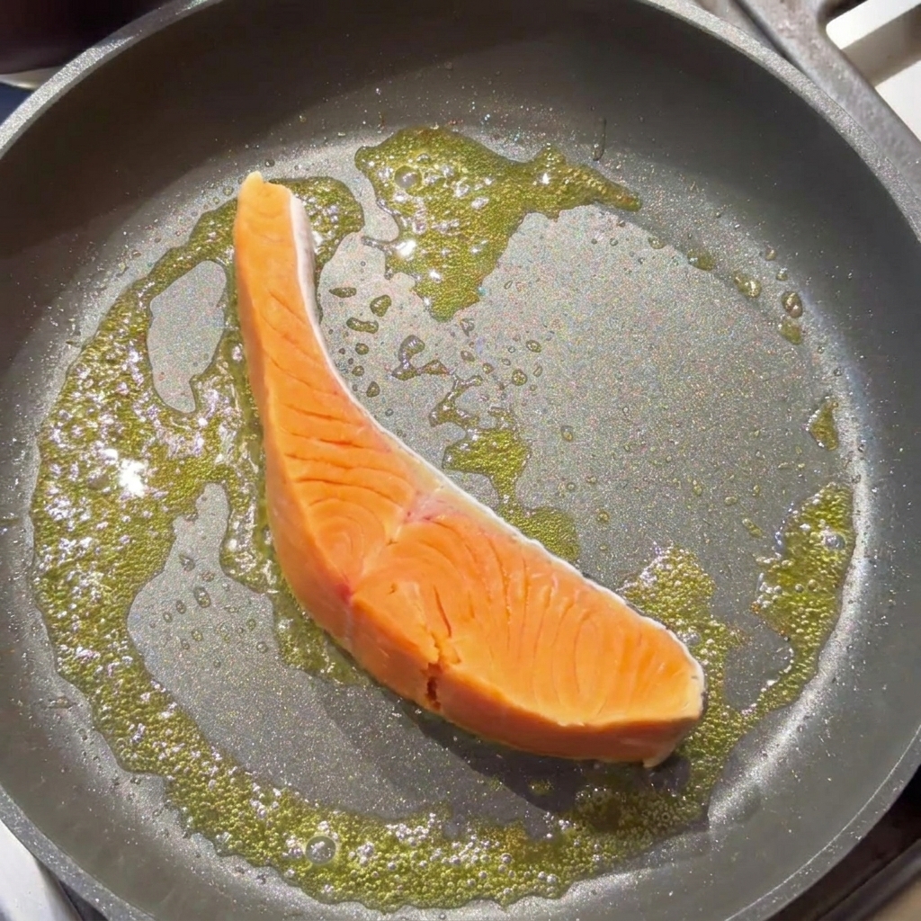 Un filete de salmón crudo sellándose en una sartén con mantequilla burbujeante.