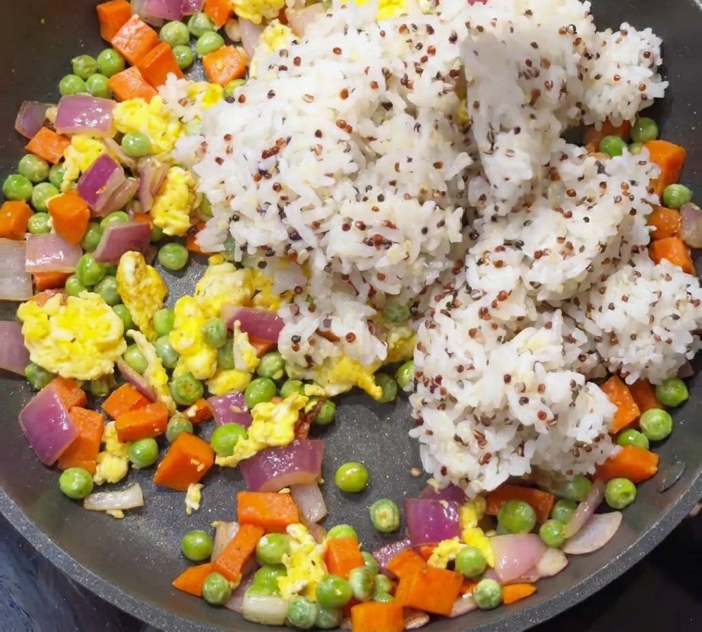 Arroz blanco y quinoa cocidos siendo añadidos a una sartén con verduras salteadas y huevos.