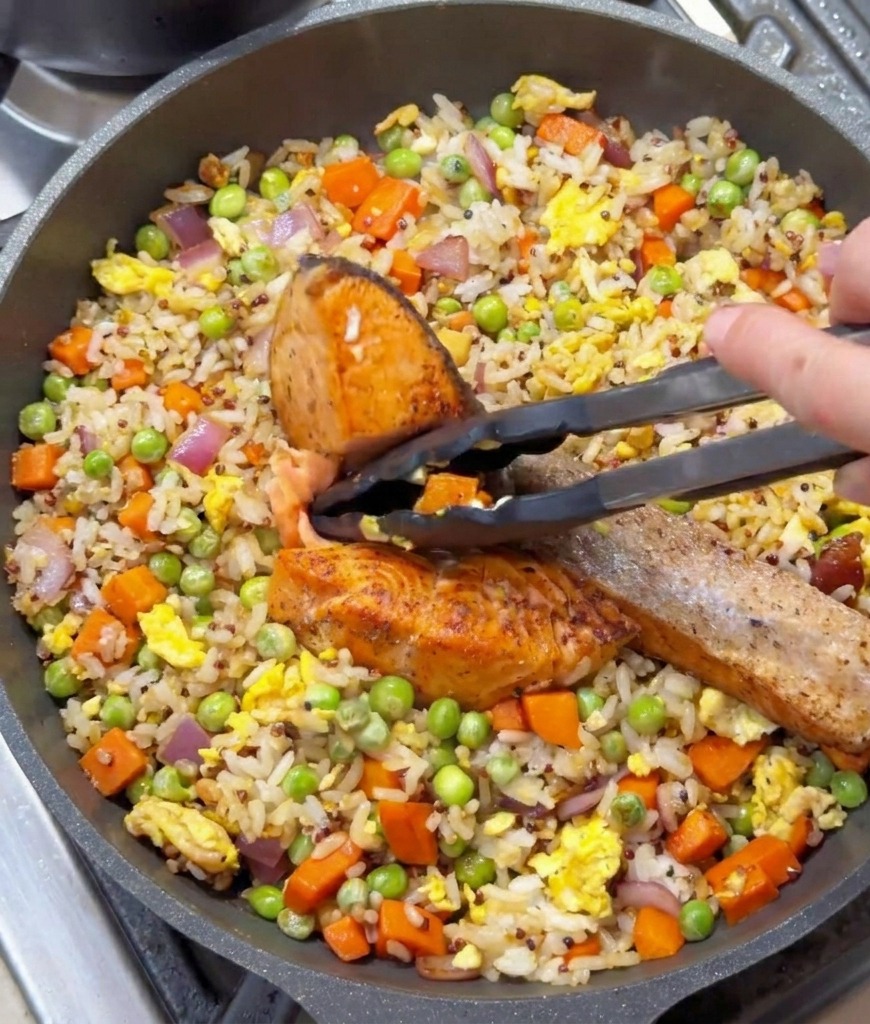 Pinzas de cocina sosteniendo un trozo de salmón sellado sobre una sartén con arroz y verduras.