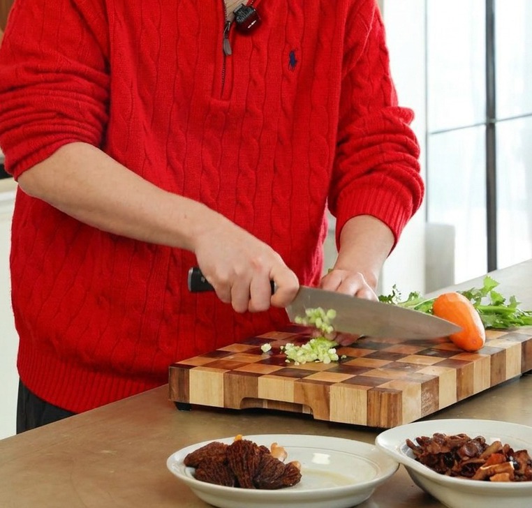 Persona usando un cuchillo profesional para picar finamente apio verde y zanahorias naranjas en una tabla de madera.