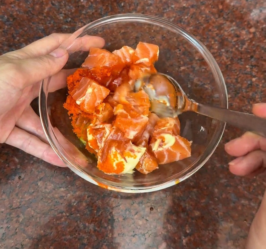 Bol de cristal con cubos de salmón mezclándose con huevas de pescado y una salsa cremosa naranja.