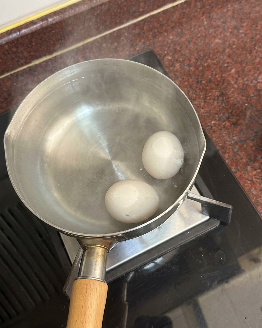 Dos huevos blancos en el fondo de una olla con agua caliente y vapor subiendo de la superficie.