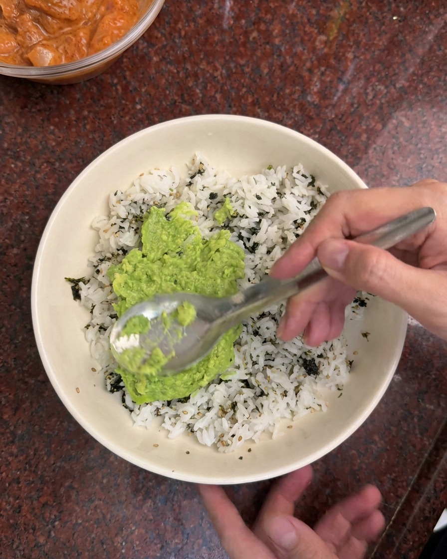 Cuchara extendiendo puré de aguacate verde sobre una base de arroz blanco y algas en un bol.