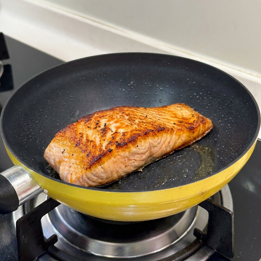 Un filete de salmón sellado en una sartén amarilla mostrando una superficie perfectamente dorada y crujiente.