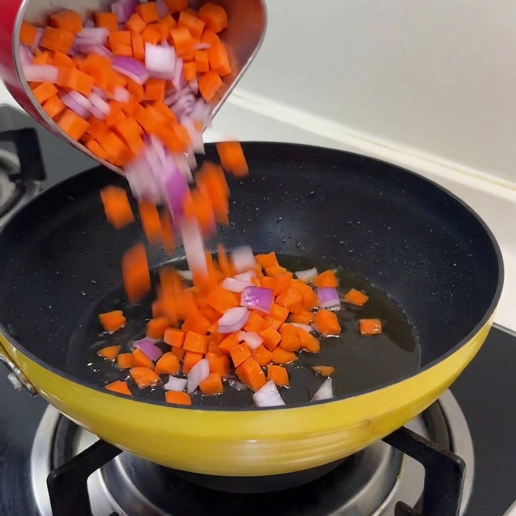 Una mezcla de zanahorias naranjas y cebollas moradas picadas vertiéndose en una sartén amarilla con aceite brillante.