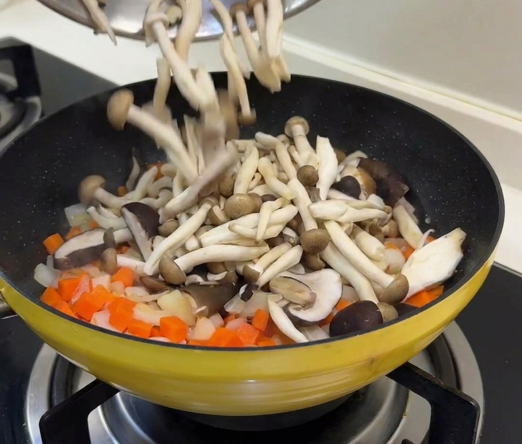 Setas frescas y guisantes vertiéndose desde un bol a la sartén con el sofrito de zanahoria y cebolla.