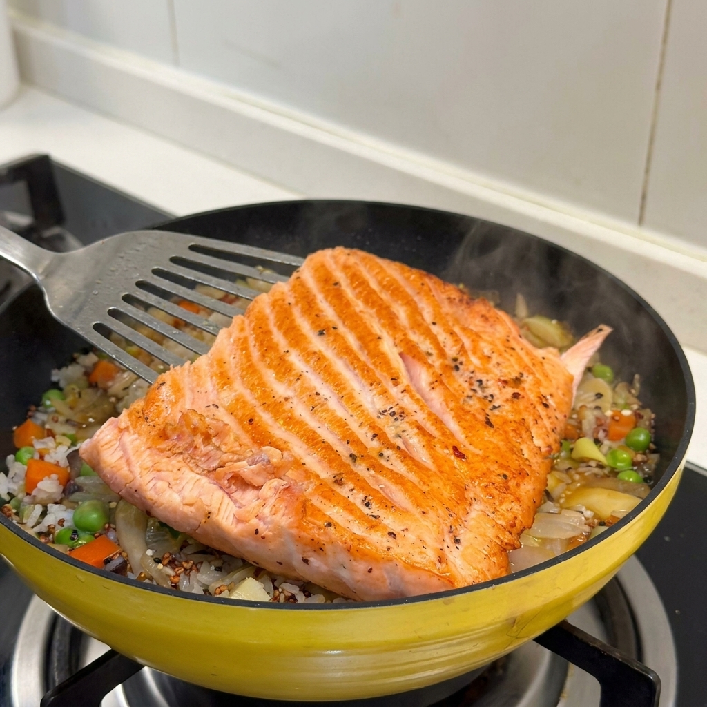 Un filete de salmón dorado colocándose sobre la cama de arroz y verduras en la sartén.
