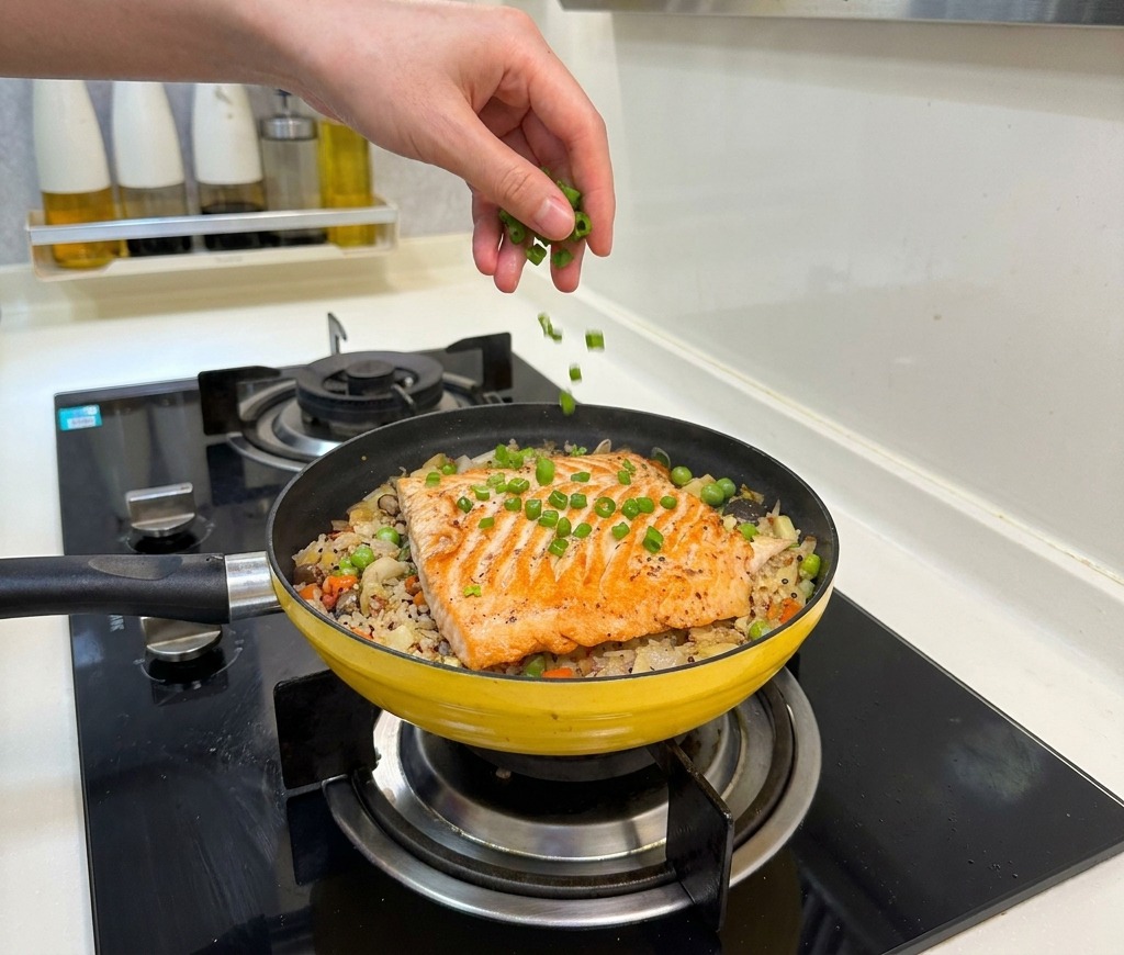 Una mano esparciendo cebolleta verde picada sobre el arroz con salmón terminado.