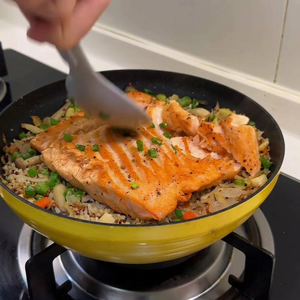 Una cuchara rompiendo el filete de salmón en lascas sobre el arroz braseado.