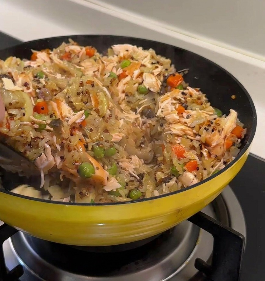 Una mano usando una espátula para integrar las lascas de salmón en el arroz con quinoa y verduras.
