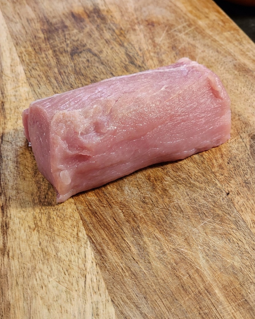 Una pieza fresca y gruesa de lomo de cerdo crudo sobre una tabla de cortar de madera.