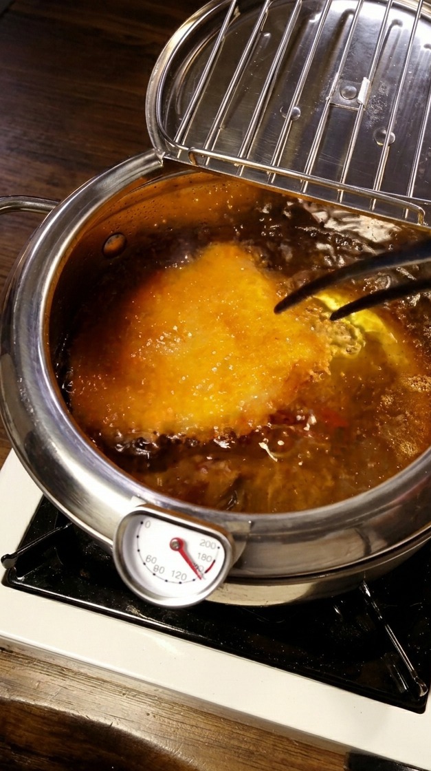 Chuleta de cerdo empanada friéndose en una olla con aceite caliente y una sonda de temperatura visible.