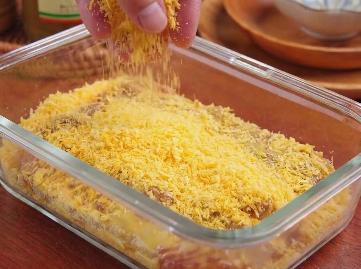Pan rallado panko amarillo siendo presionado sobre la superficie de una chuleta de cerdo en una fuente de vidrio.