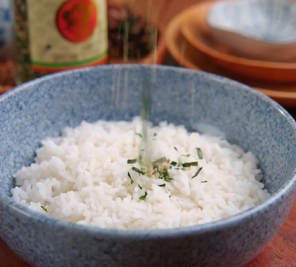 Tiras de alga nori siendo espolvoreadas en el centro de un bol azul lleno de arroz blanco.