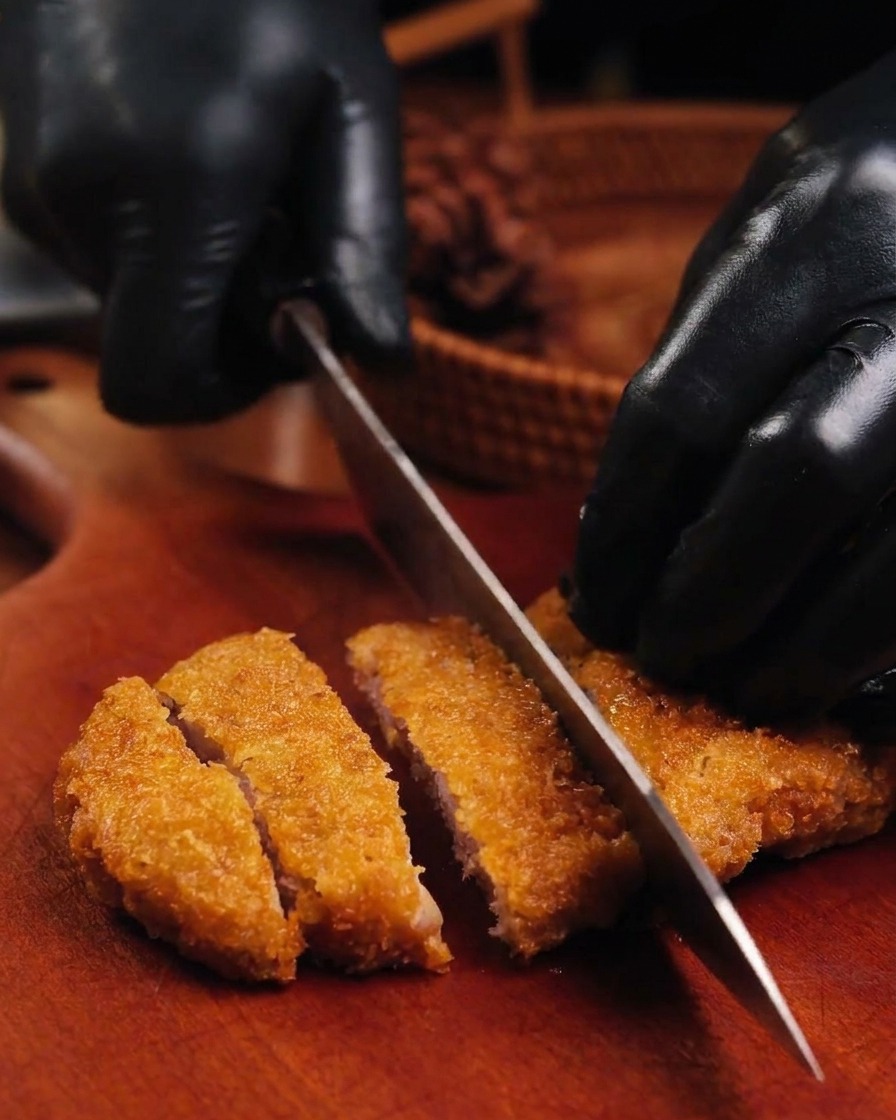 Cuchillo afilado cortando una chuleta de cerdo dorada y crujiente sobre una tabla de madera.