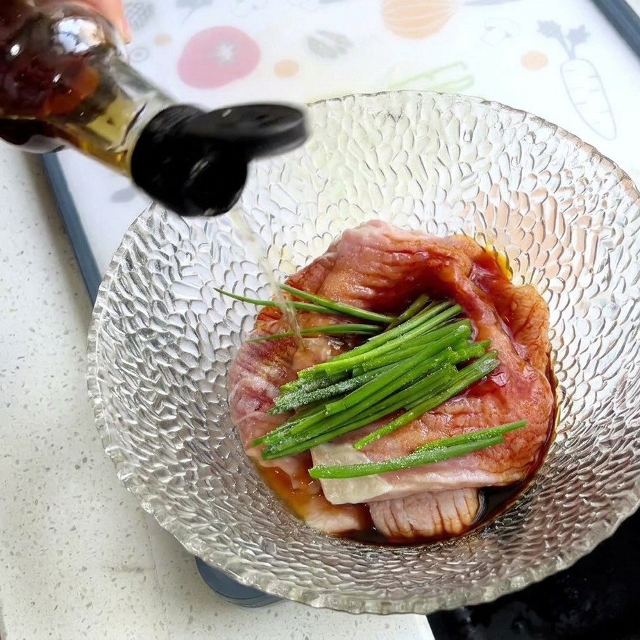 Mano vertiendo condimentos desde una botella en un bol con cerdo crudo, cebolletas verdes y almidón blanco