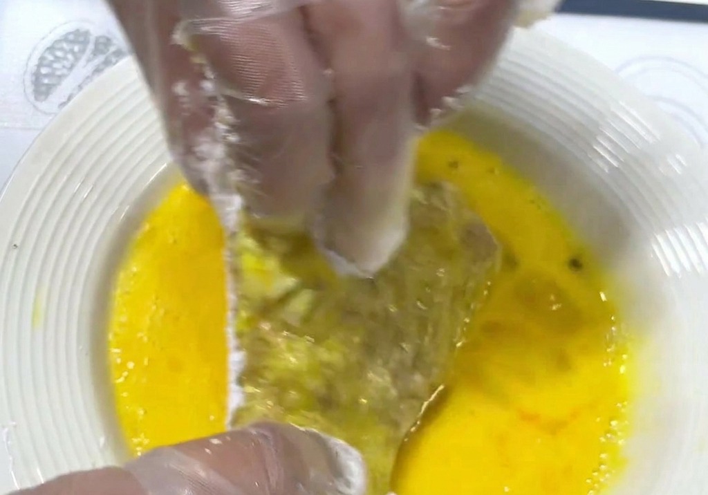 Manos sumergiendo una chuleta de cerdo con almidón en un plato hondo con huevo batido de color amarillo intenso