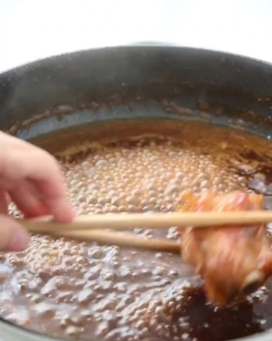 Contramuslos de pollo hirviendo en una salsa de miel oscura y burbujeante con vapor subiendo.