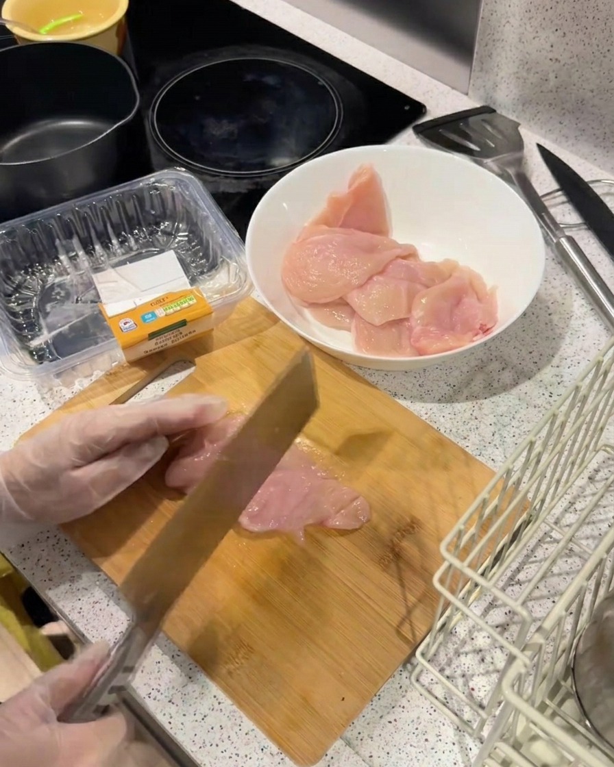 El lomo de un cuchillo pesado golpeando un filete de pollo sobre una tabla de madera para aplanarlo.