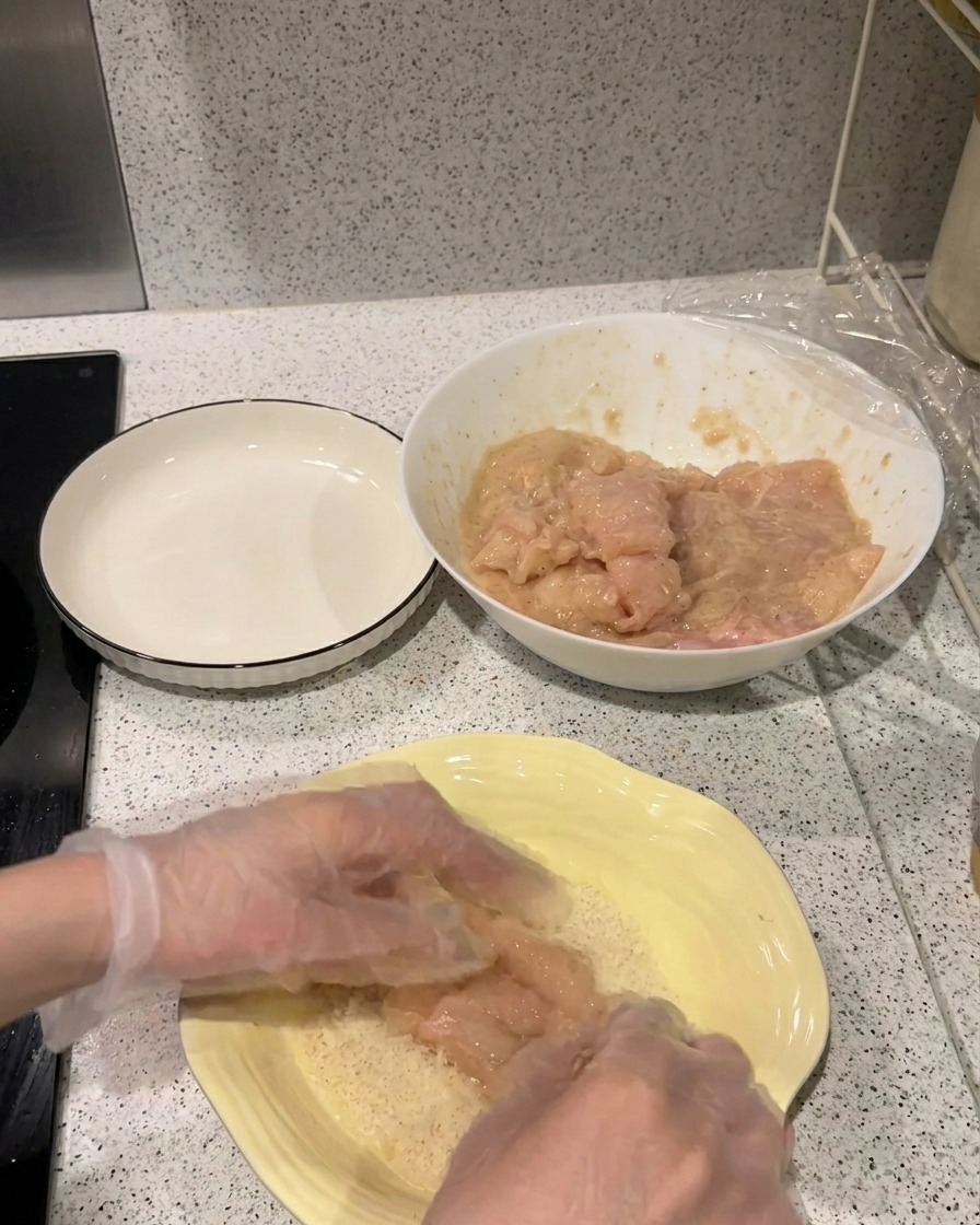 Un filete de pollo marinado presionándose contra un plato con pan rallado Panko de color claro.