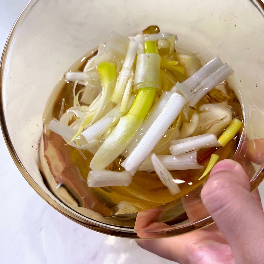 Primer plano de un bol con agua, trozos de cebolleta verde y rodajas de jengibre fresco.