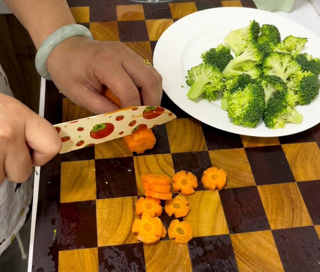 Manos usando un cuchillo para cortar una zanahoria acanalada en discos decorativos con forma de flor sobre una tabla de cortar.