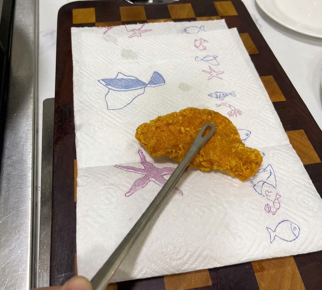 Un filete de pollo frito crujiente y dorado descansando sobre una toalla de papel blanca con patrones azules de vida marina para escurrirse.