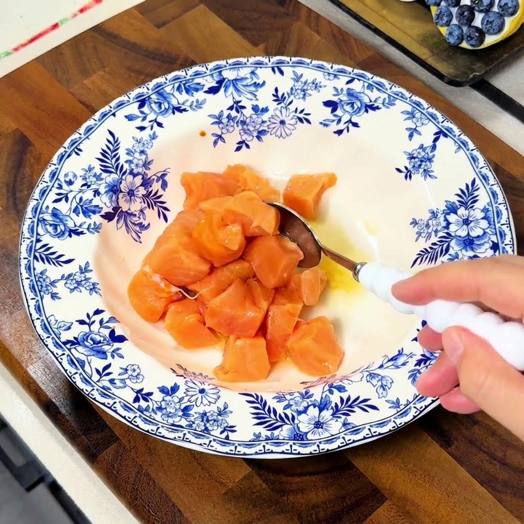 Una mano removiendo los dados de salmón con una cuchara blanca en un tazón azul y blanco para que queden bien cubiertos por la marinada.