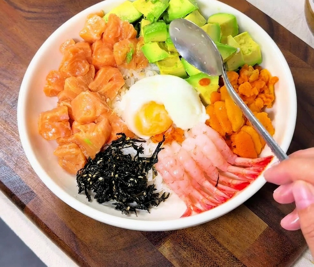 Una cuchara colocando un huevo onsen blanco en el centro de los coloridos ingredientes del tazón.