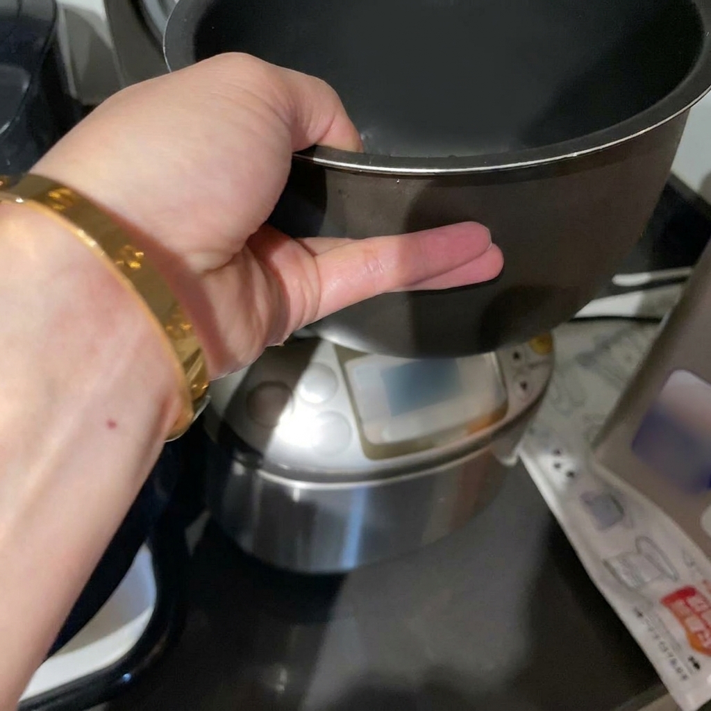 Una mano sosteniendo la olla de una arrocera con arroz blanco crudo sumergido en agua.