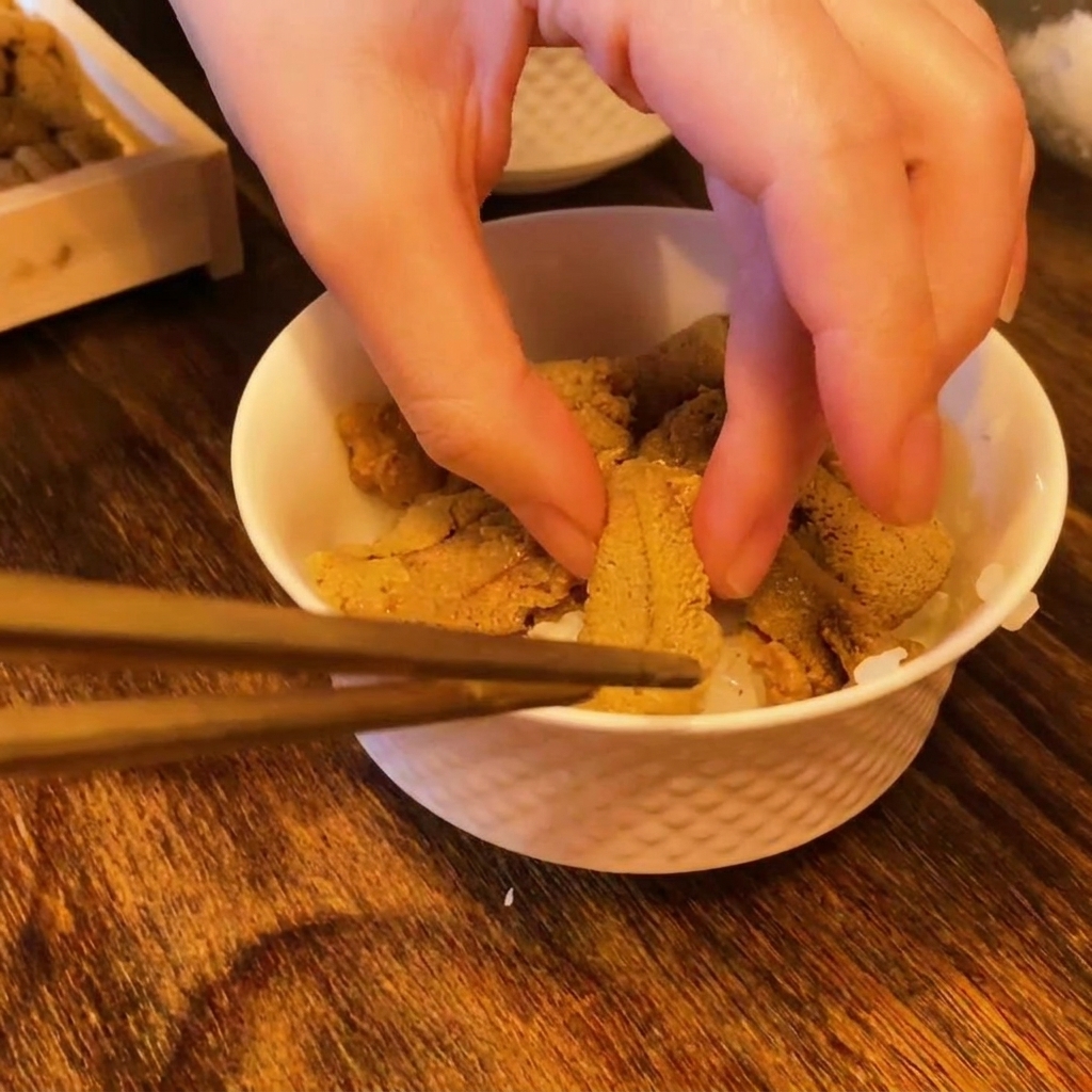 Palillos colocando trozos de erizo de mar naranja brillante sobre una cama de arroz para sushi en un tazón.