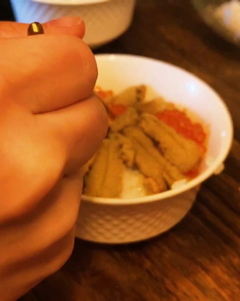Primer plano de una mano usando una cuchara pequeña para rellenar los huecos de un tazón de erizo con huevas de salmón.