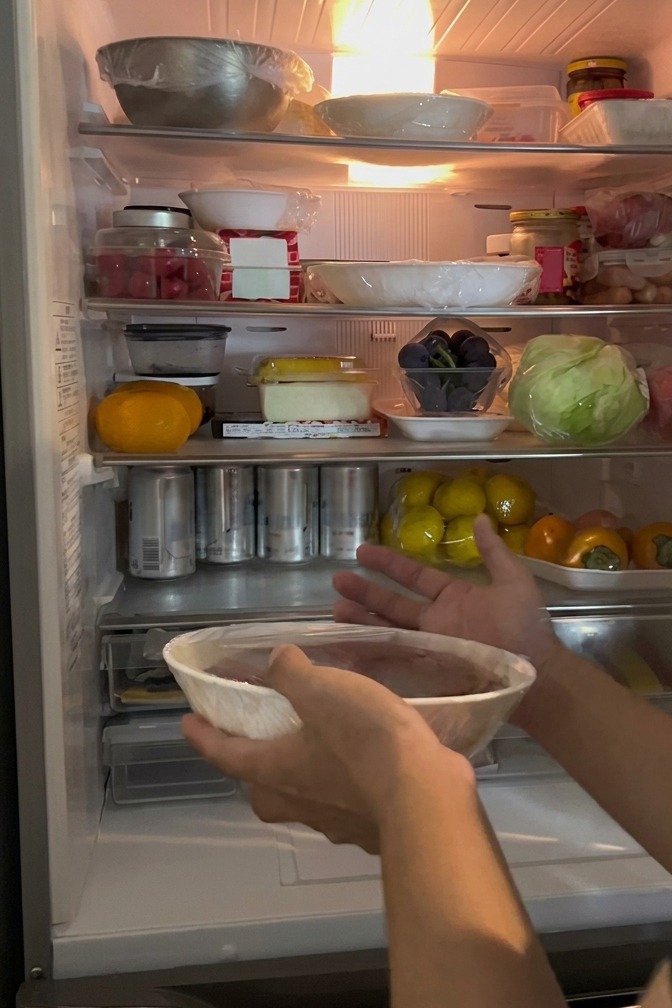 Mano colocando un bol de huevas de salmón sellado con film transparente en el frigorífico.