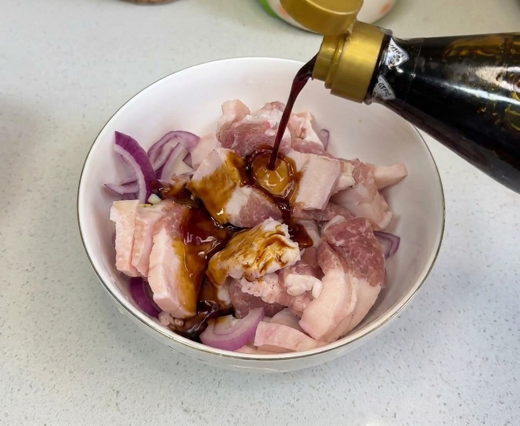 Salsa de soja oscura vertiéndose desde una botella sobre la carne y la cebolla en un cuenco.