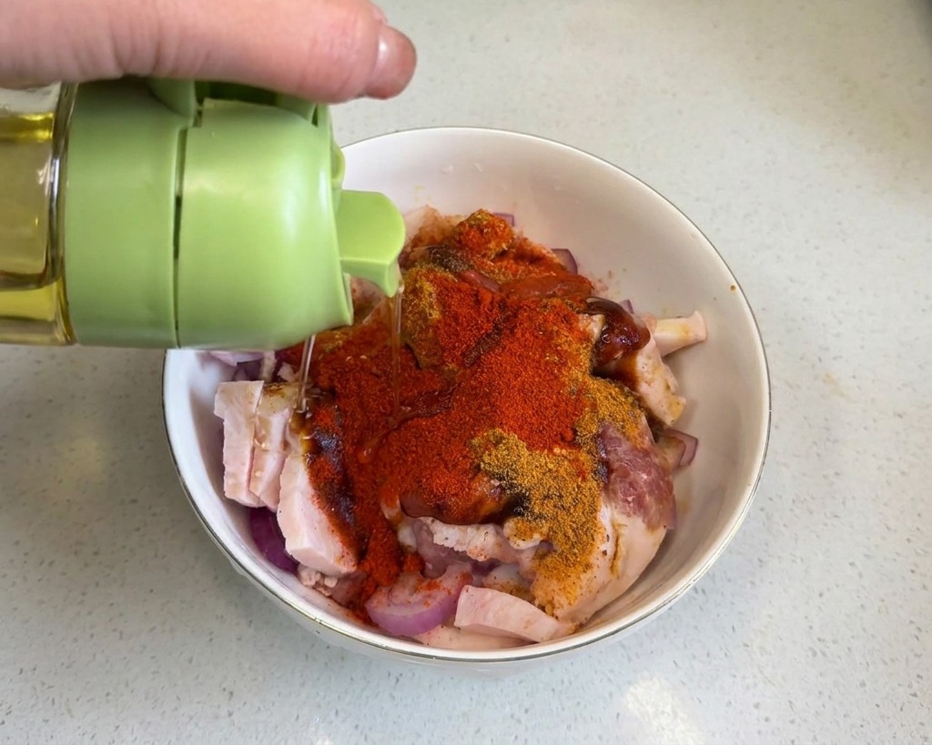 Aceite de cocina vertiéndose sobre la panceta cubierta de especias rojas.