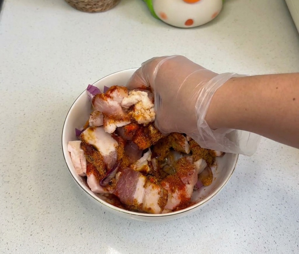 Una mano mezclando bien la panceta, las cebollas y los condimentos en un cuenco blanco.