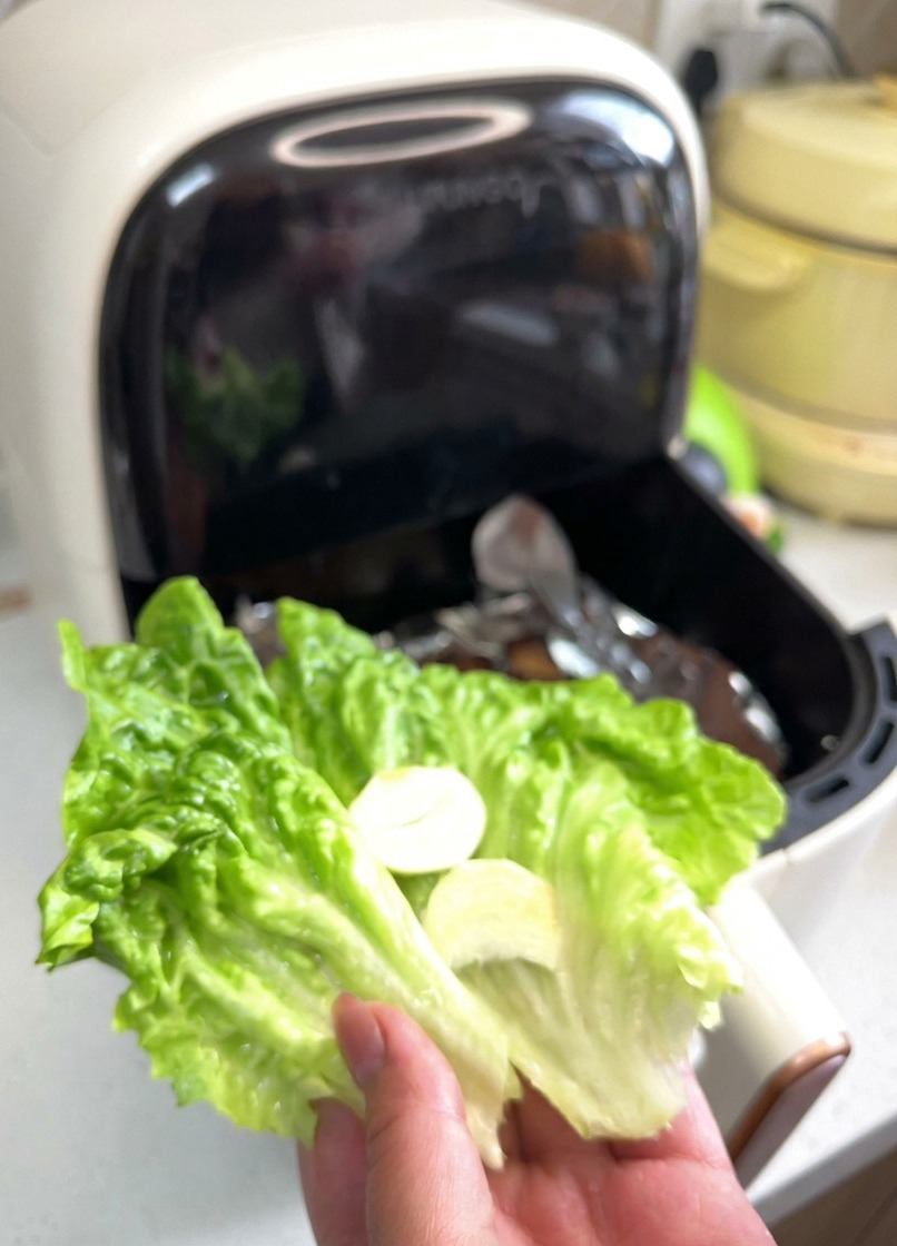 Una mano sosteniendo una hoja de lechuga verde con láminas de ajo y aros de cebolla encima.