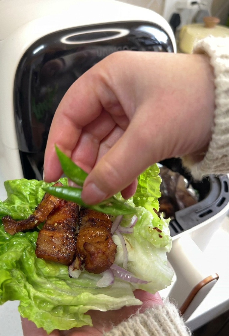 Una mano poniendo rodajas de chile verde sobre un wrap de lechuga con panceta.