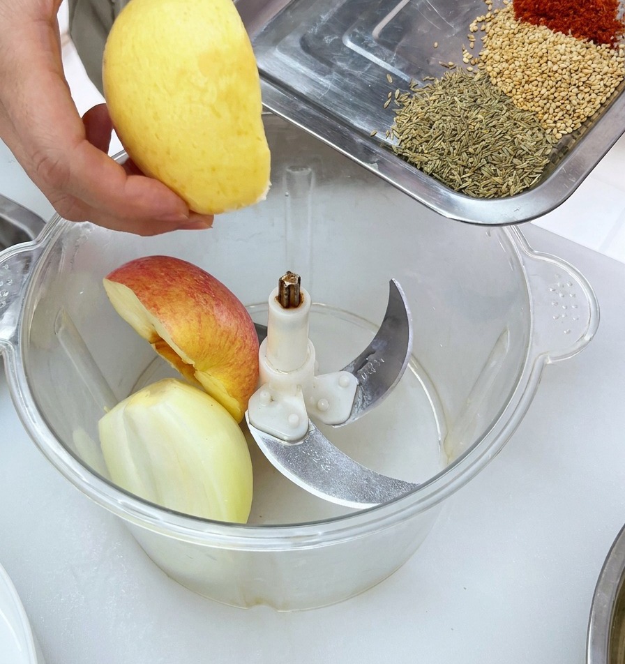 Trozos de fruta fresca colocados en el vaso de un procesador de alimentos junto a las especias listas para mezclar.