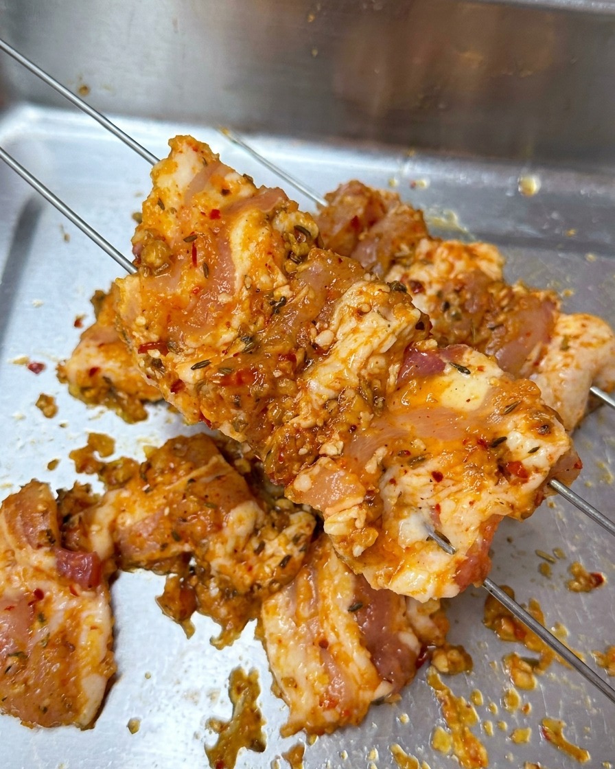 Lonchas de panceta marinada atravesadas por dos brochetas metálicas finas sobre una bandeja de preparación.