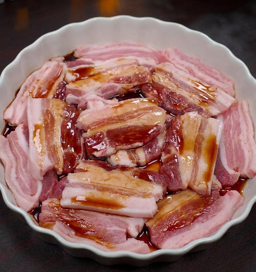 Rodajas de panceta cruda en un plato blanco cubiertas con un marinado oscuro.