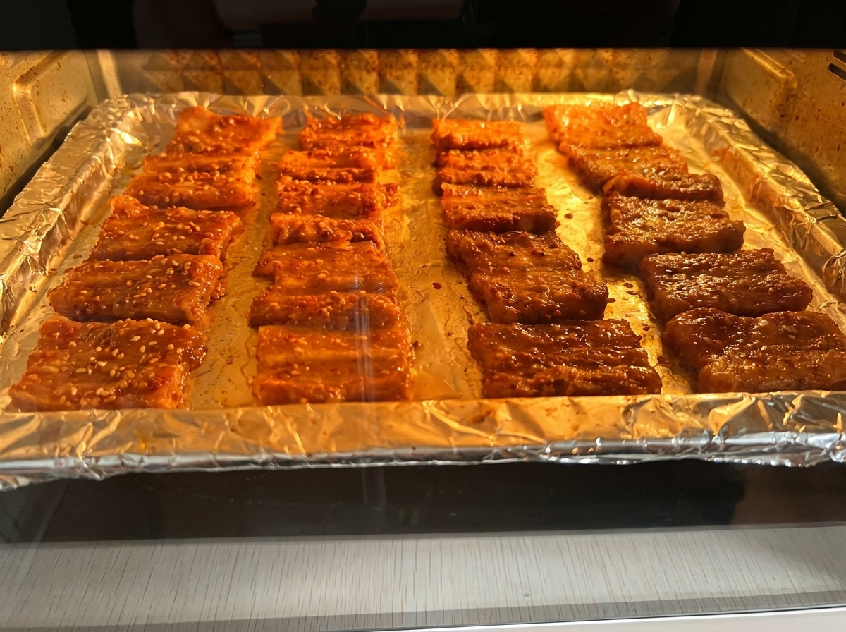 Rodajas de panceta marinada asándose en una bandeja dentro de un horno iluminado.