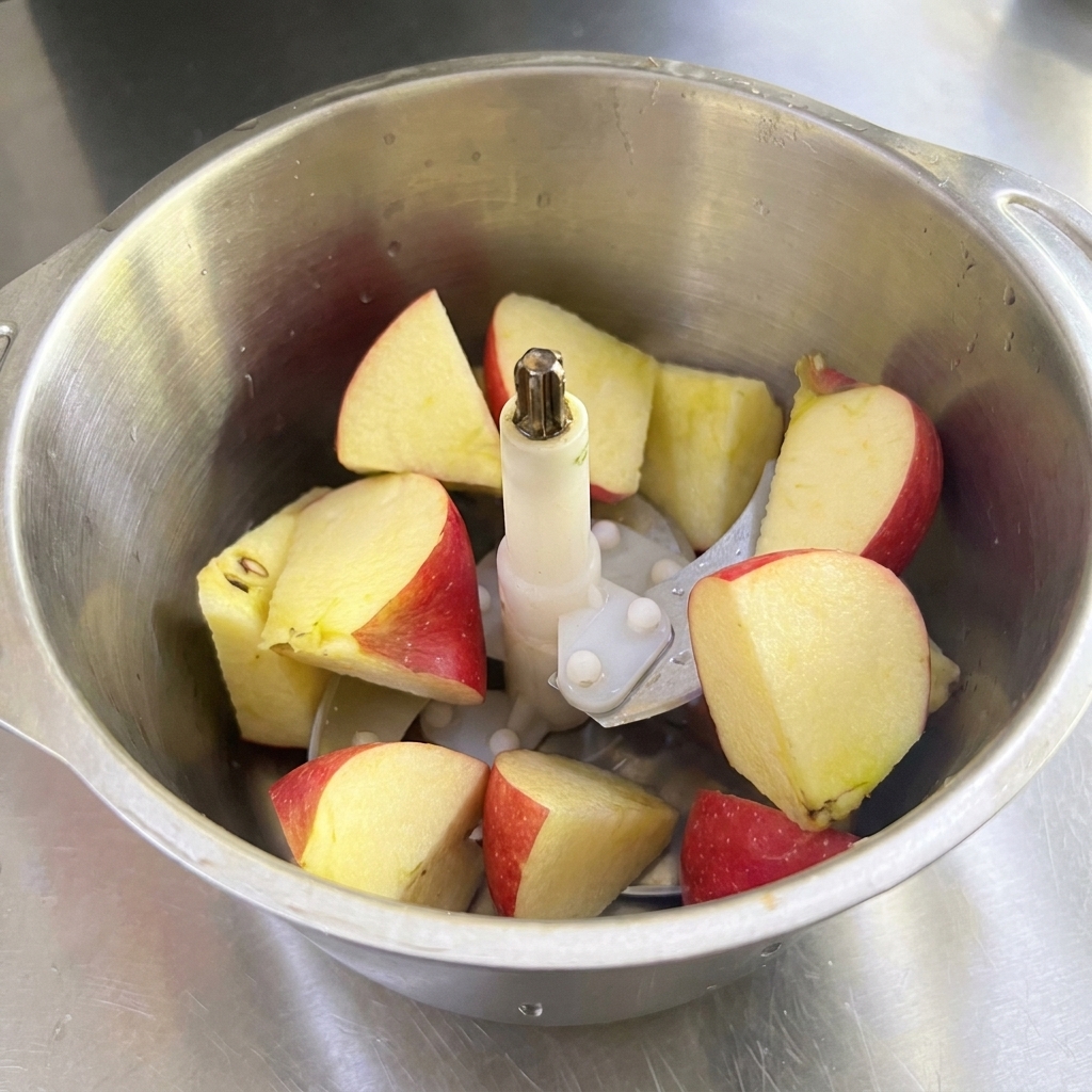 Una jarra de batidora de acero inoxidable llena de trozos grandes de manzana roja, pera y cebolla blanca.