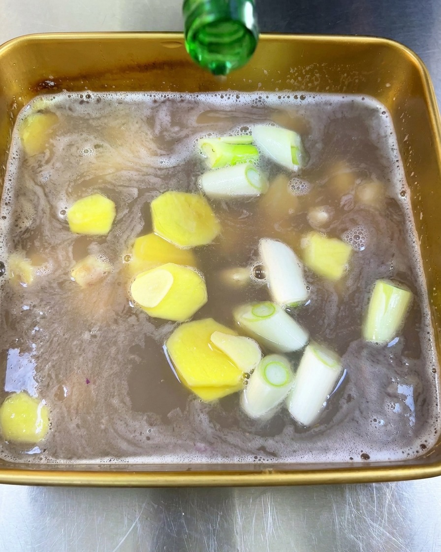 Vino de arroz transparente vertiéndose desde una botella de vidrio verde en una bandeja con adobo líquido.