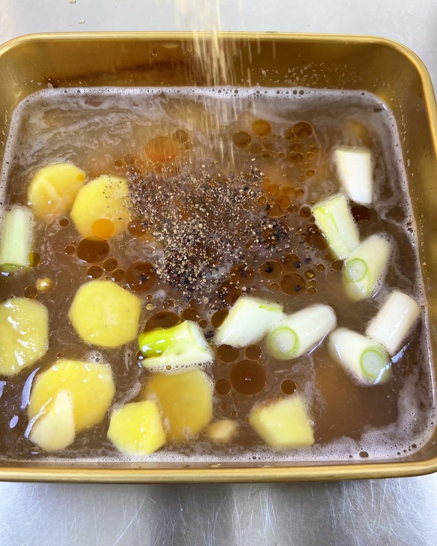 Pimienta negra molida espolvoreada sobre un adobo líquido con gotas de aceite y vegetales aromáticos.