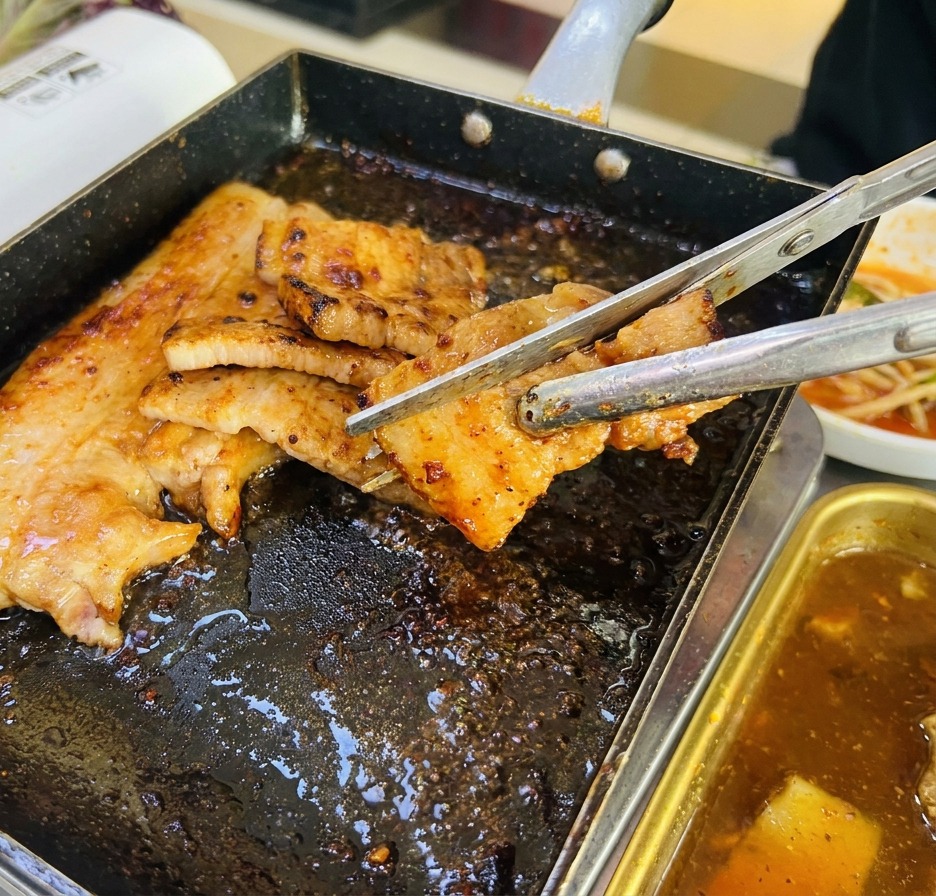 Primer plano de lonchas de panceta siendo cortadas con tijeras de cocina sobre una plancha caliente.