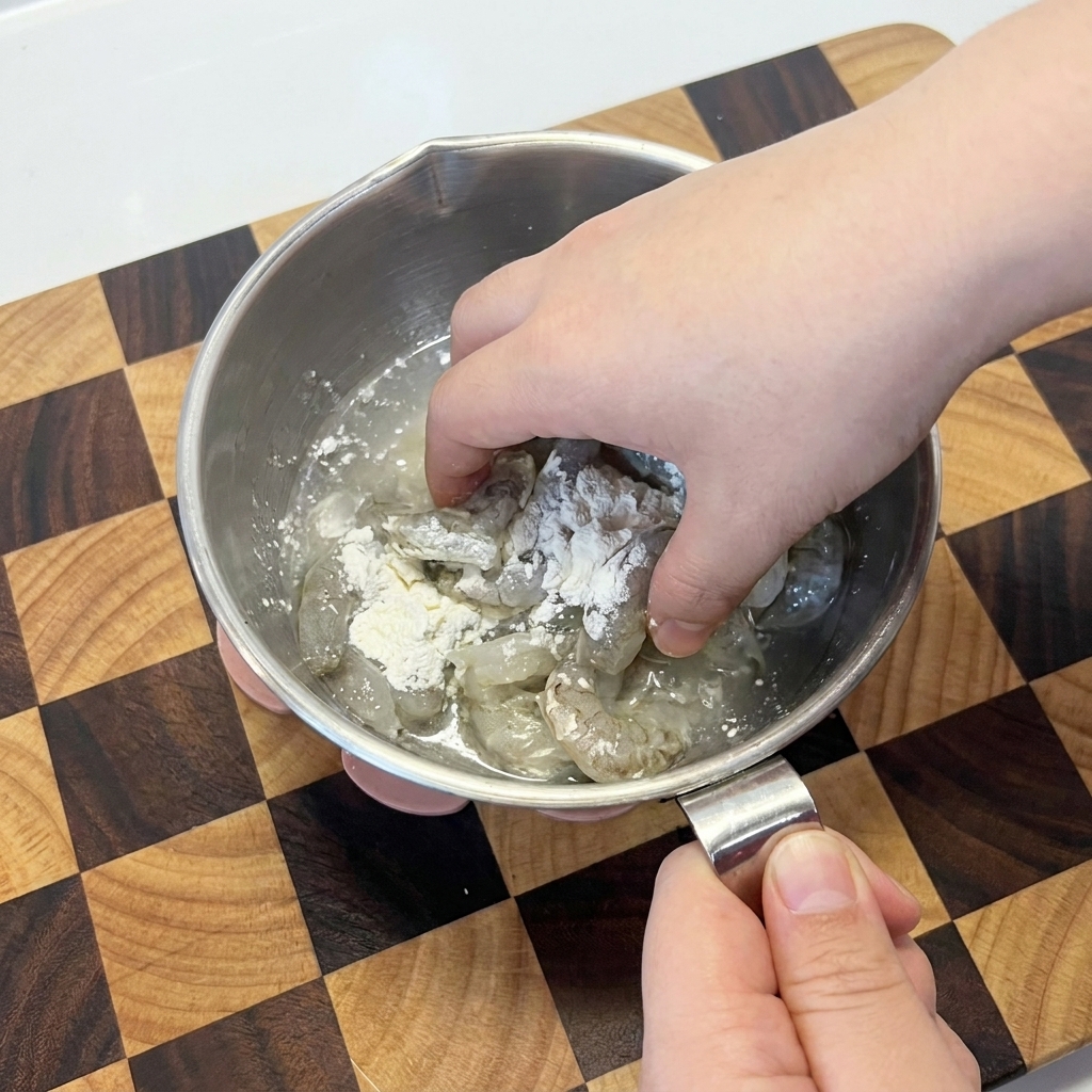 Camarones crudos mezclándose con almidón de maíz blanco a mano en un bol metálico.
