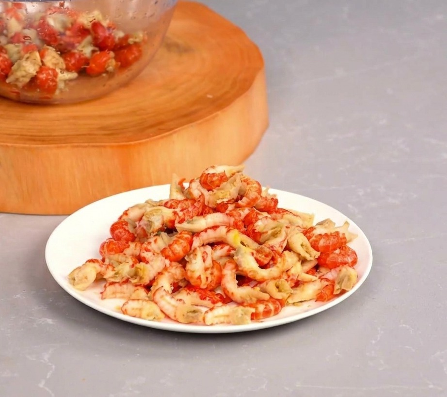 Un plato blanco con una montaña de colas de cangrejo peladas junto a un cuenco de cristal sobre una tabla de madera.